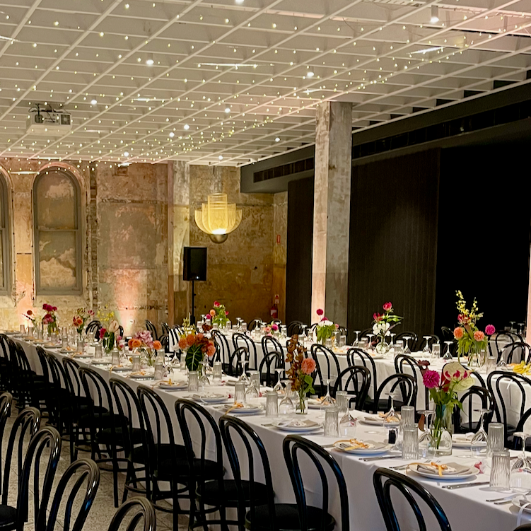 Dining hall with long tables set for a formal event, featuring floral centerpieces and black chairs.